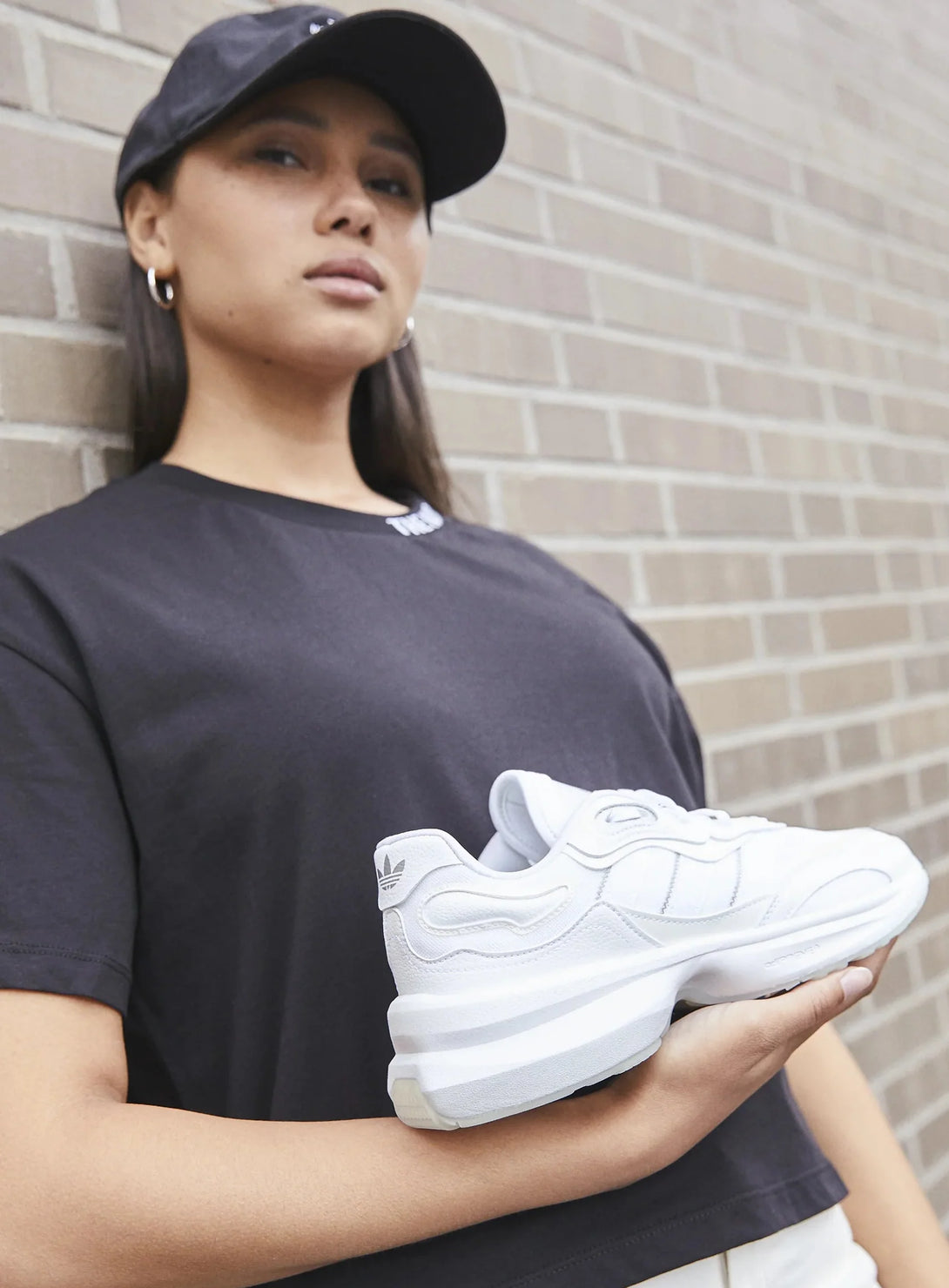adidas Originals ZENTIC White held by a model against a brick wall, showcasing its stylish design.